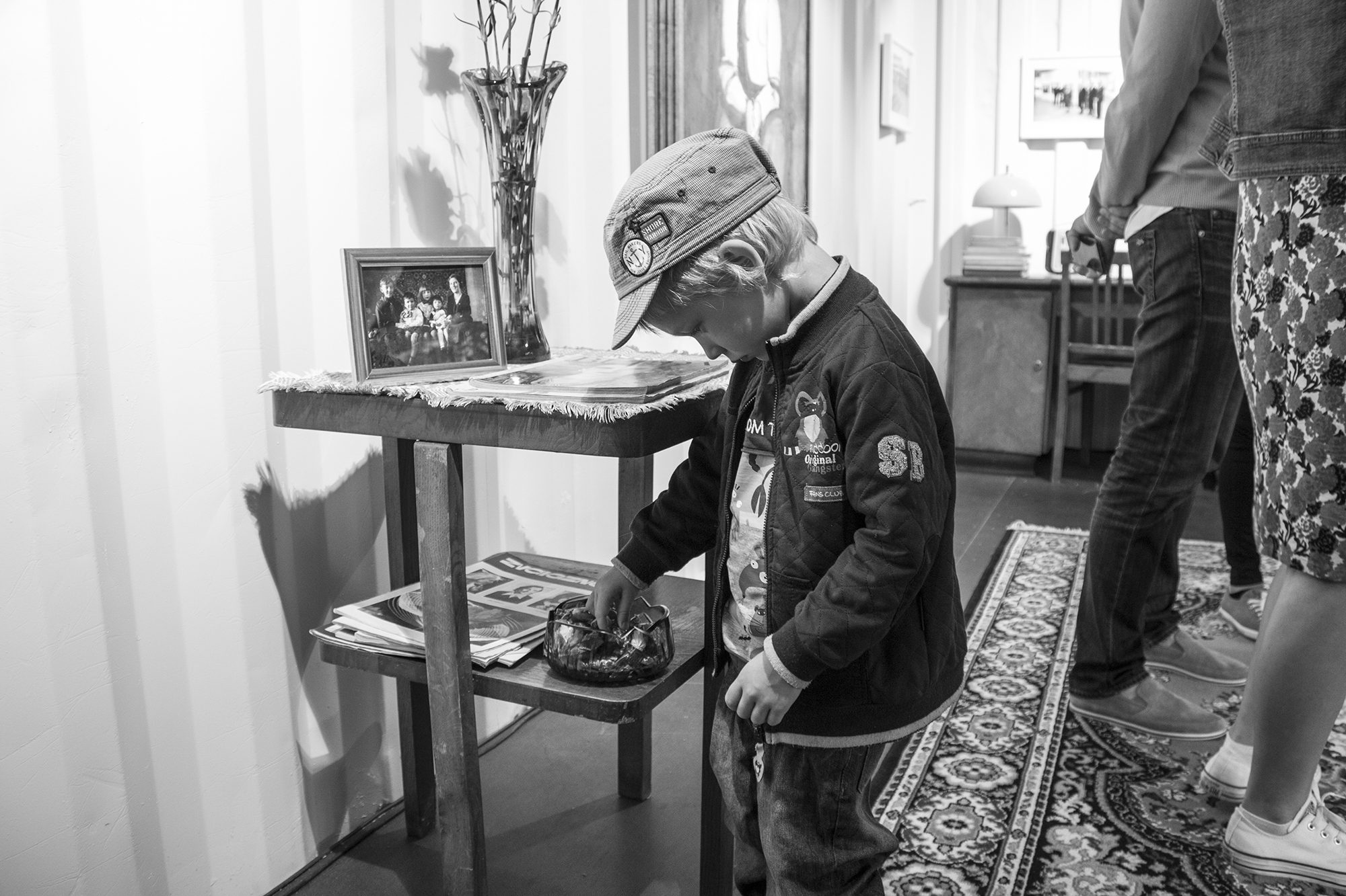Galdiņš ar ierāmētu ģimenes fotogrāfiju un žurnāliem; puisis cepurē aplūko priekšmetus