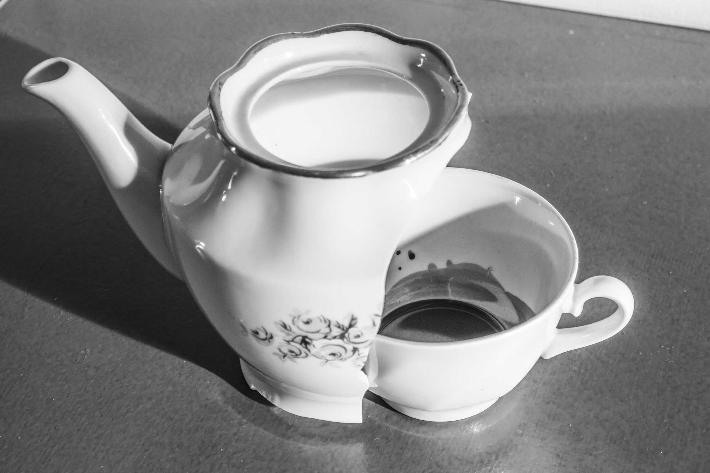 Porcelāna tējkanna un saplīsusi tase ar tumšu šķidrumu uz grīdas