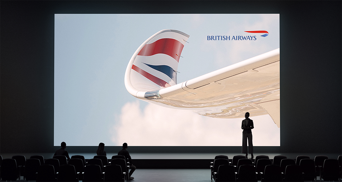 People sitting in a theater watching a British Airways airplane tail with logo on screen.