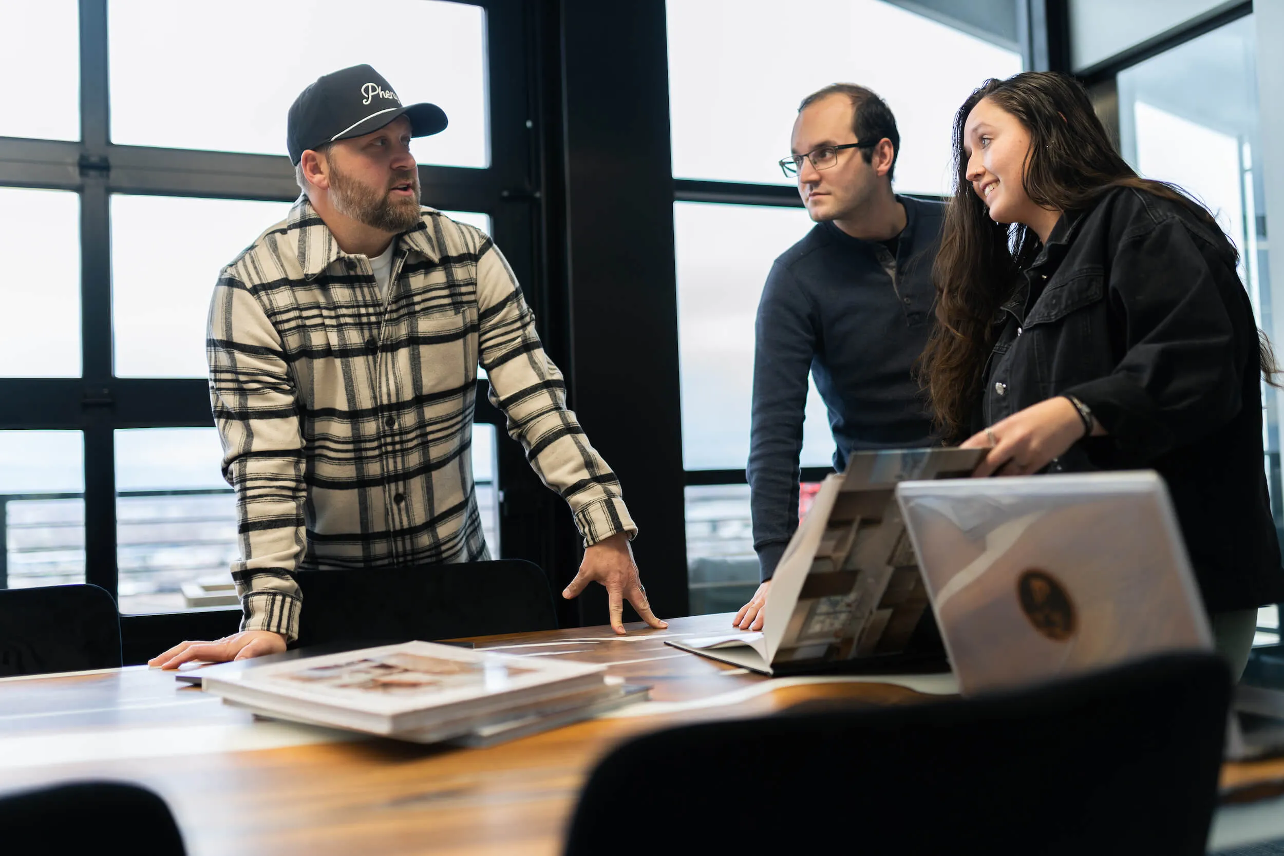 Three PHENYX team members reviewing printed brand books and photo proofs on a conference table by a window