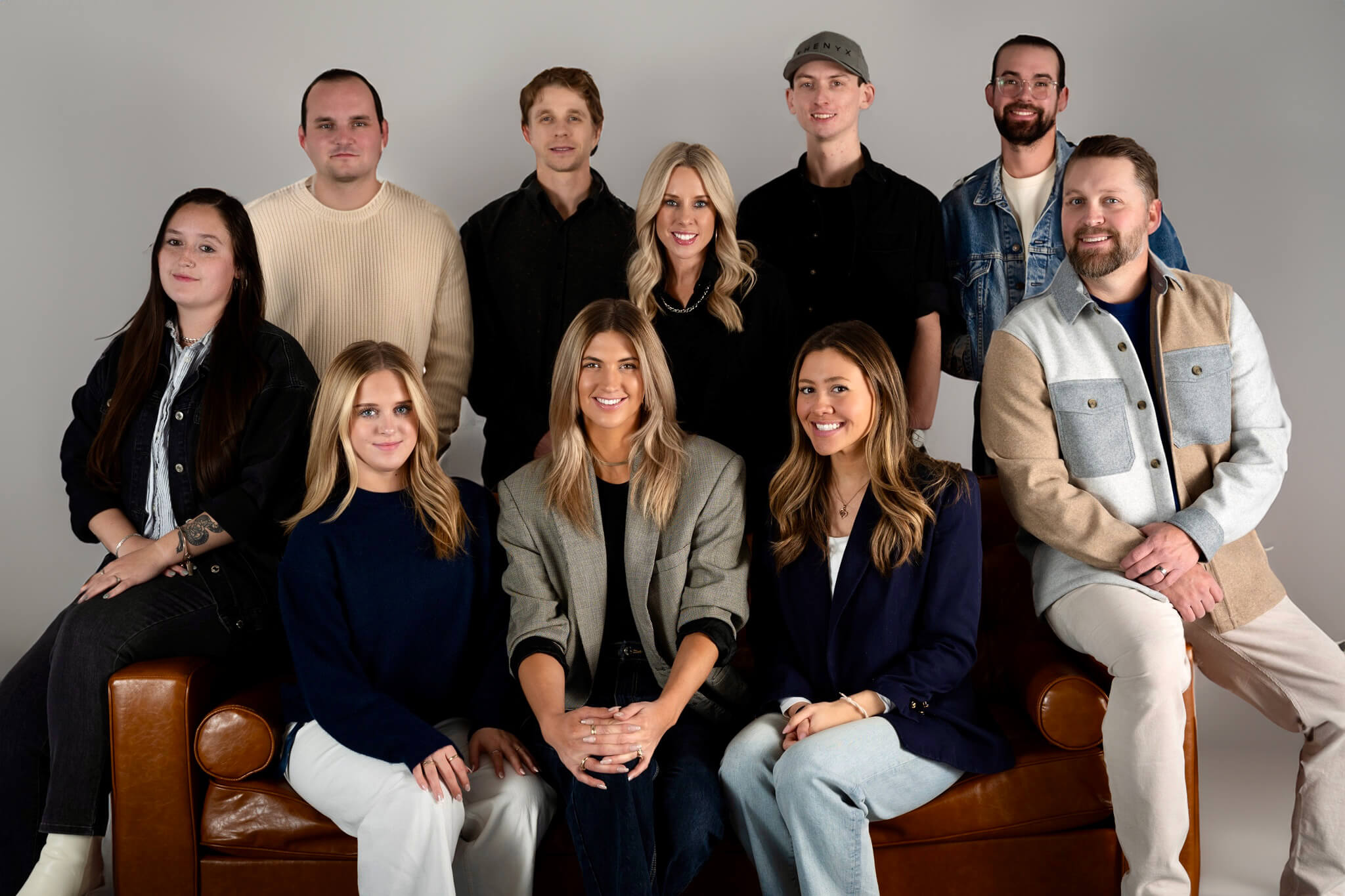 Studio group portrait of the ten-person PHENYX team seated on a leather sofa against a grey backdrop