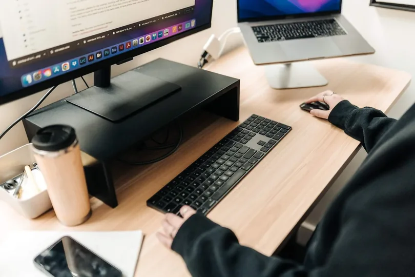 Close-up of a PHENYX team member typing at a desk with a keyboard, monitor and laptop