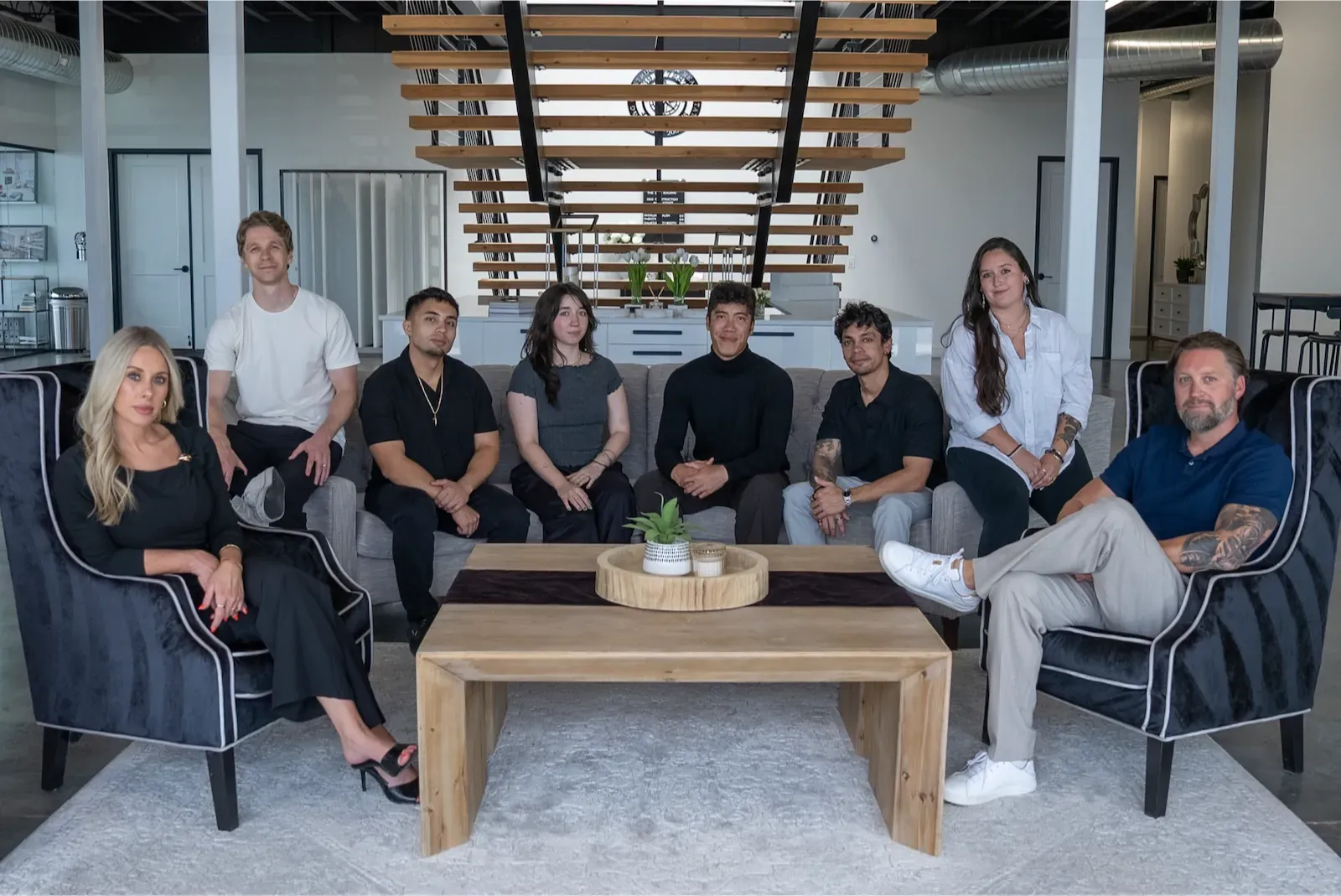 The PHENYX team of eight seated together in the studio lounge beneath a slatted wood ceiling