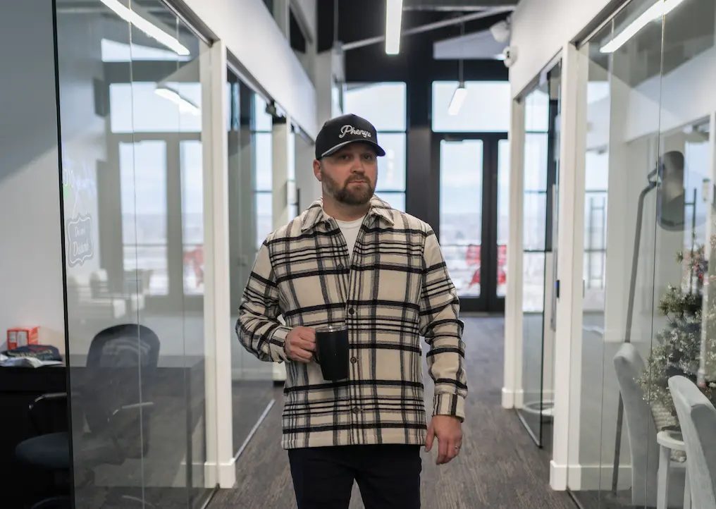 Man in a flannel shirt and Phenyx marketing hat walking in an office