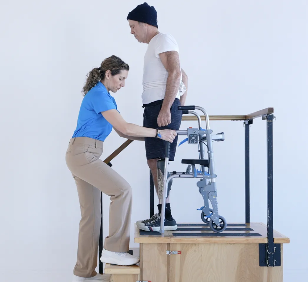A man with a leg prosthesis using the StairAssist Walker on a training step while a therapist steadies him with a gait belt
