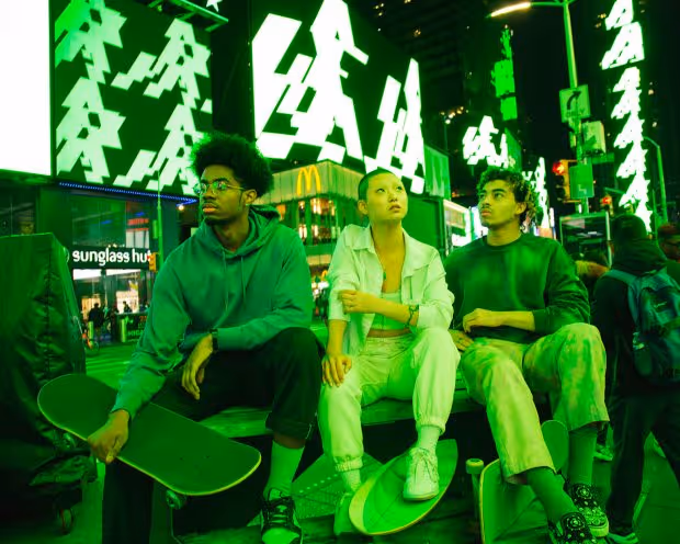 THREE INDIVIDUALS SIT ON BENCH LOOKING UP AT ALGORAND’S NEON GREEN CARBON-NEGATIVE BLOCKCHAIN INSTALLATION CALLED LIGHTS OUT AT TIMES SQUARE