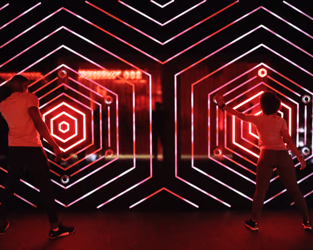 TWO INDIVIDUALS STAND NEXT TO EACH OTHER AS THEY PLACE THEIR HANDS ON A RED LINED WALL AT UNDER ARMOUR RUSH LAB