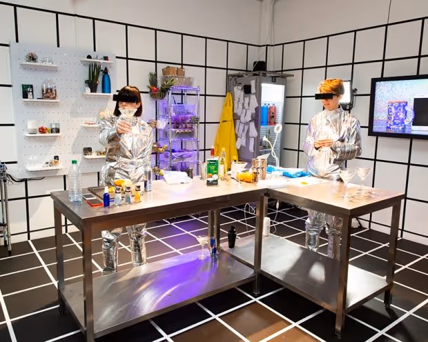 TWO INDIVIDUALS MAKE COCKTAILS IN FUTURISTIC KITCHEN THAT RESEMBLES A LAB IN EAT TECH KITCHEN