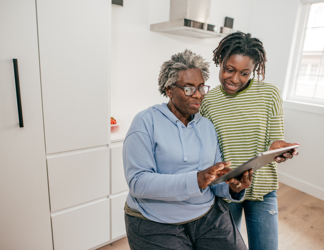 An adult daughter showing a tablet to her mother at home