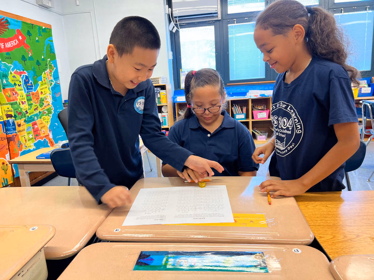 Three PS 304 students collaborating on a worksheet at their desks