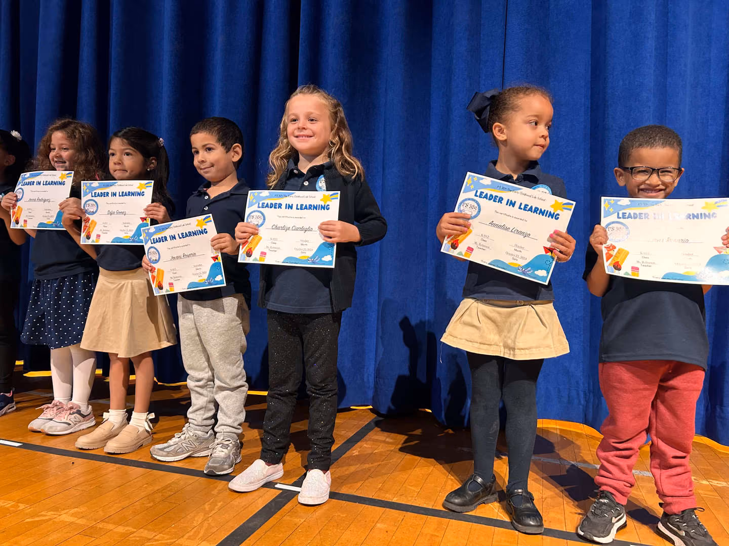 Students holding Leader in Learning certificates on stage at assembly