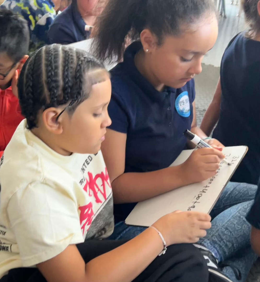 Two students working together writing on a shared clipboard