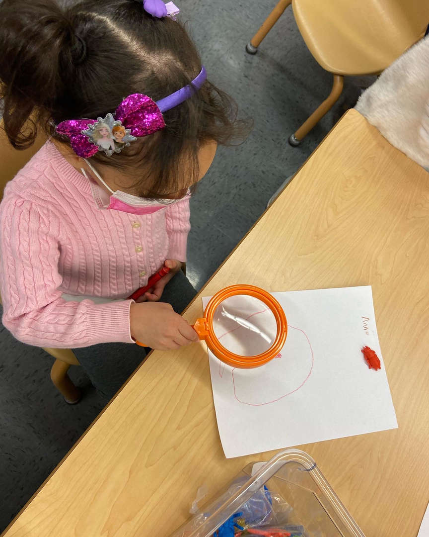 Young student using a magnifying glass to examine her drawing