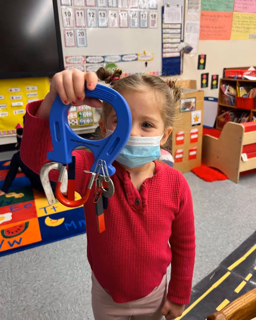 Student holds blue magnet with metal objects attached during science activity