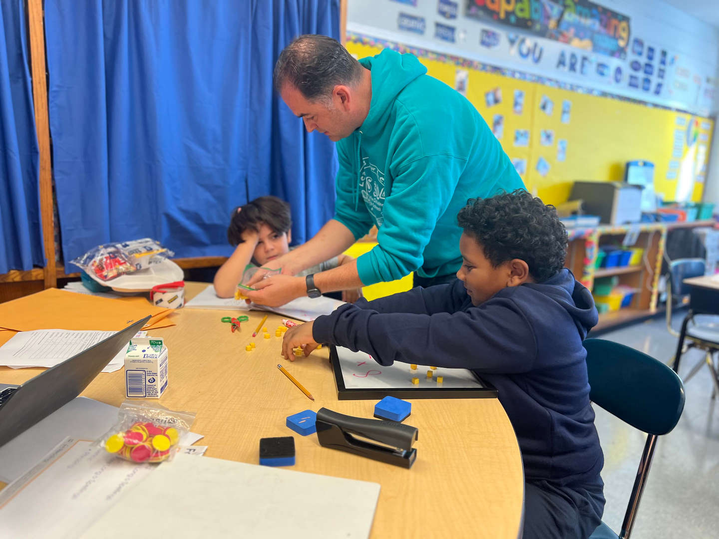 Teacher helping two students with hands-on math manipulatives at classroom table