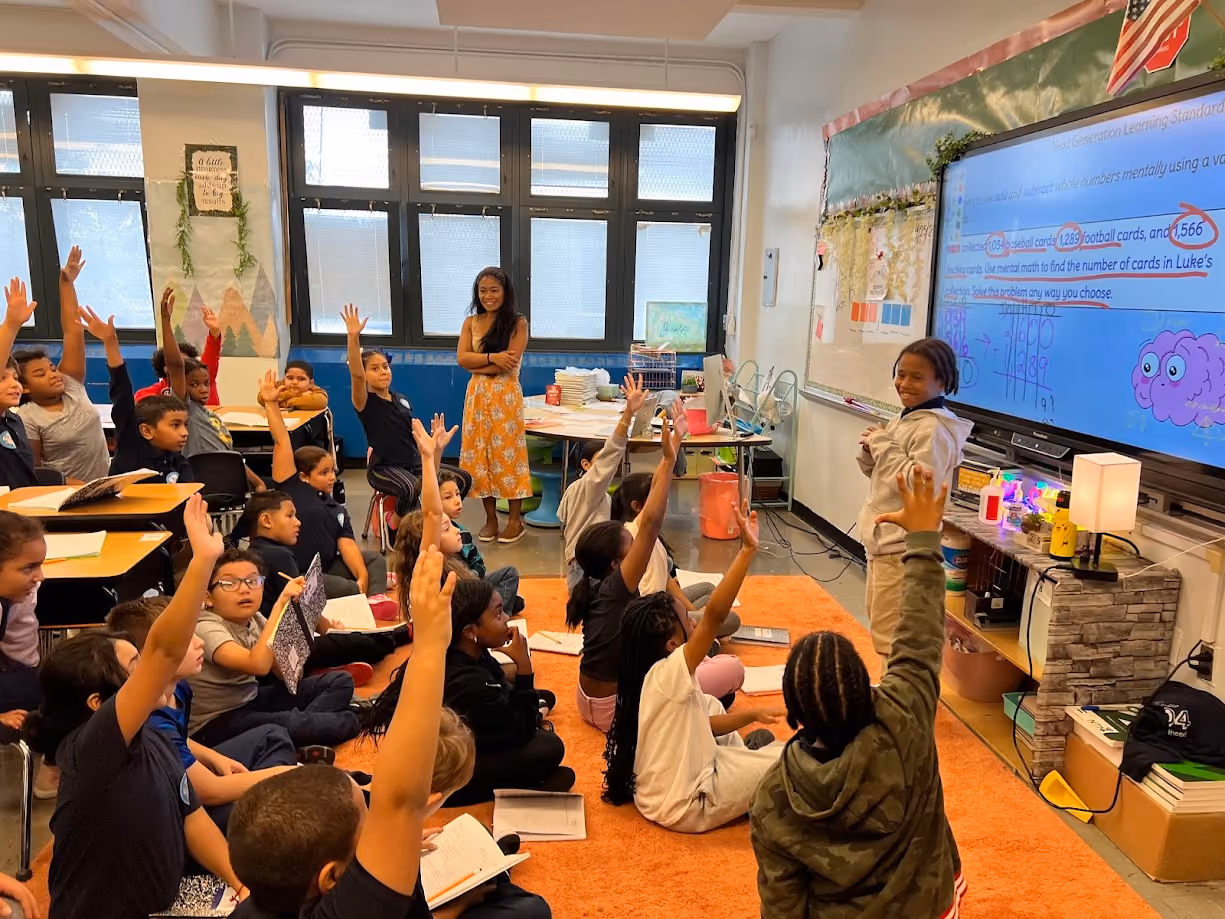 Students raising hands during interactive math lesson on smartboard
