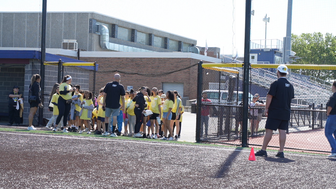 Students in yellow shirts gathered at a baseball field with staff