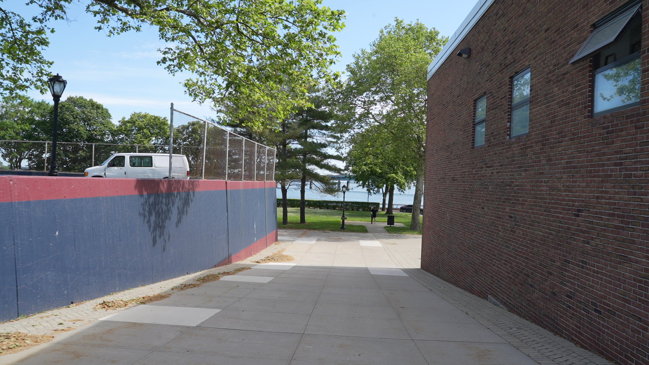 Outdoor walkway beside school building with ball field wall