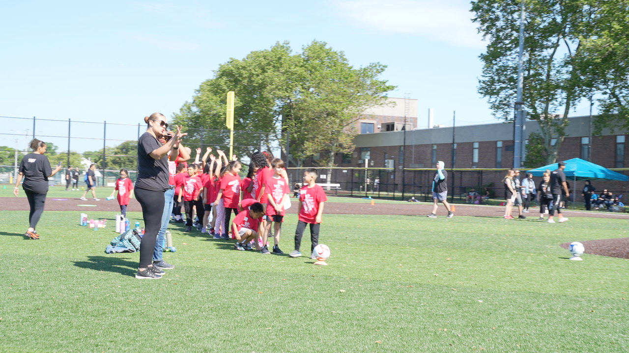 Students in red shirts gather on field during outdoor soccer activity
