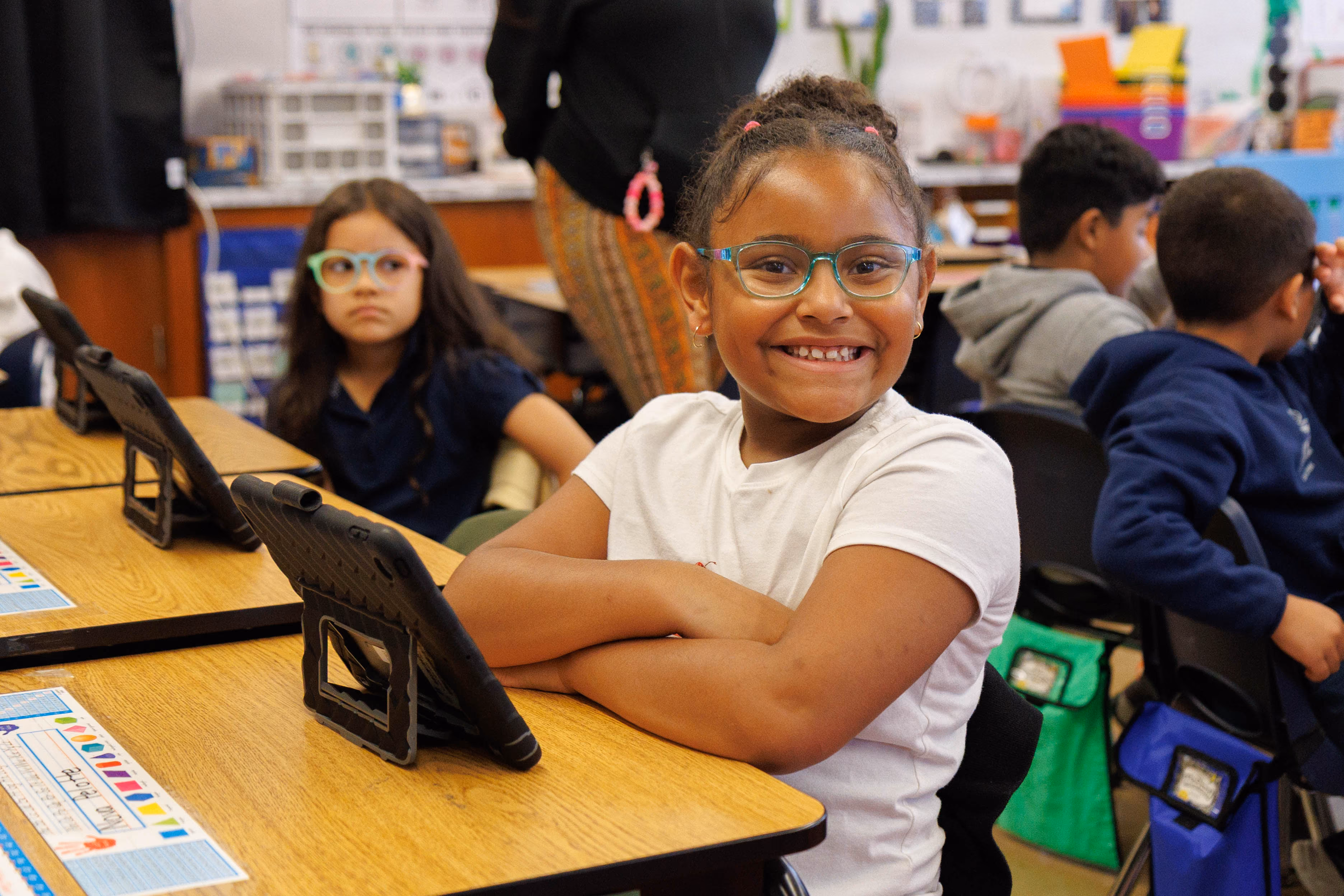 Smiling elementary student with glasses using a tablet at her desk