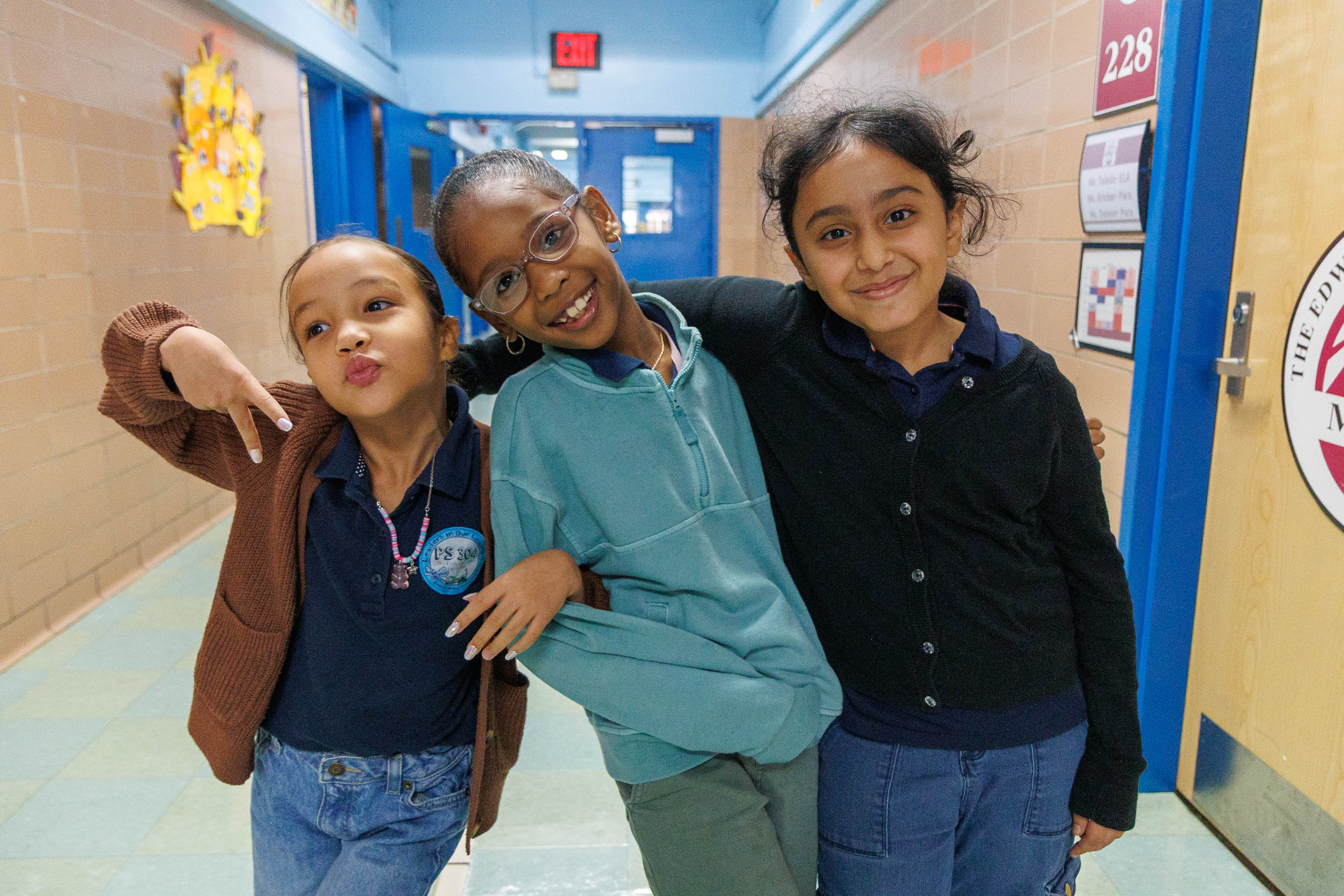 Three smiling students posing together in a school hallway