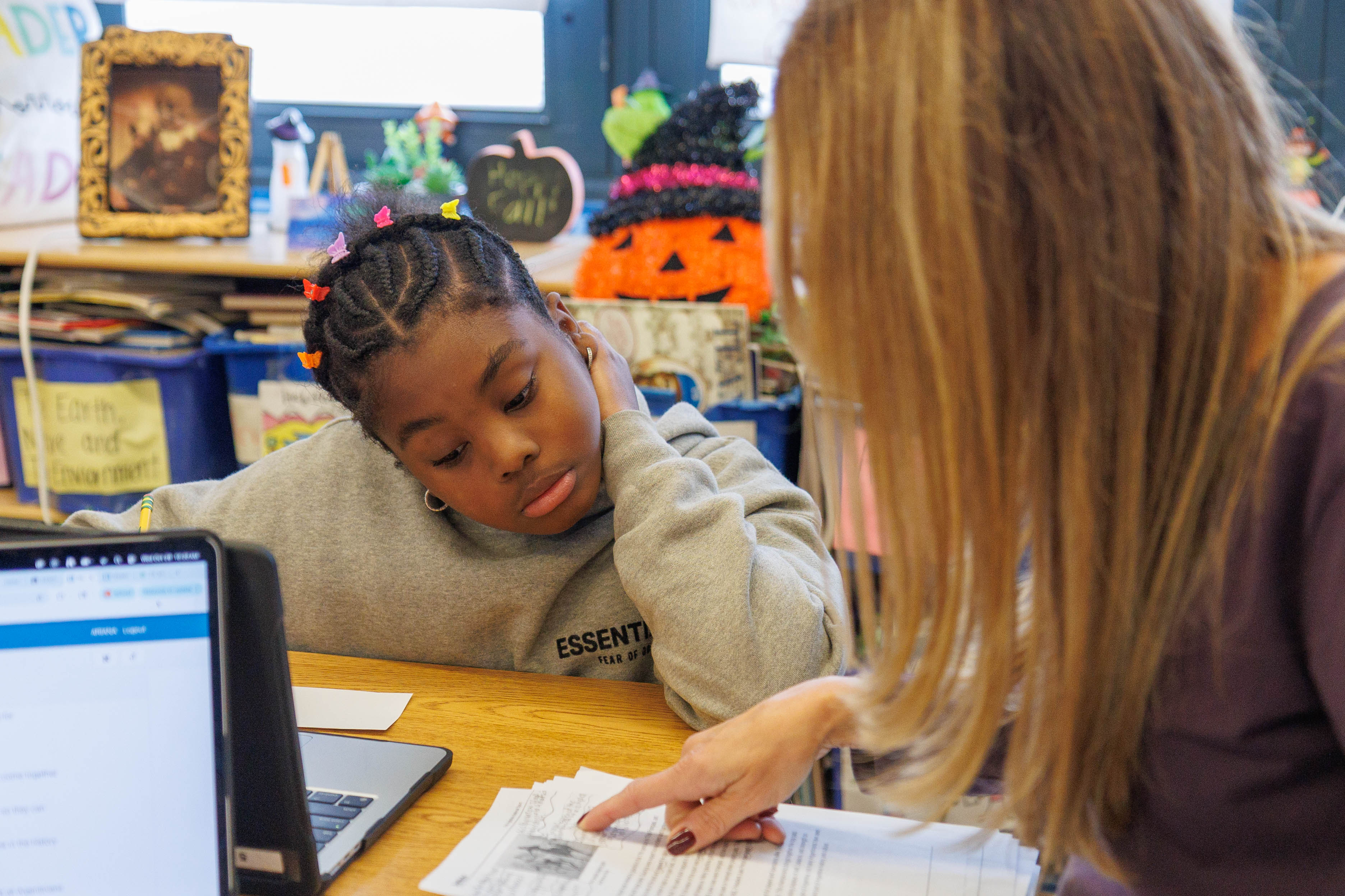 Teacher pointing to text while student reads at classroom desk