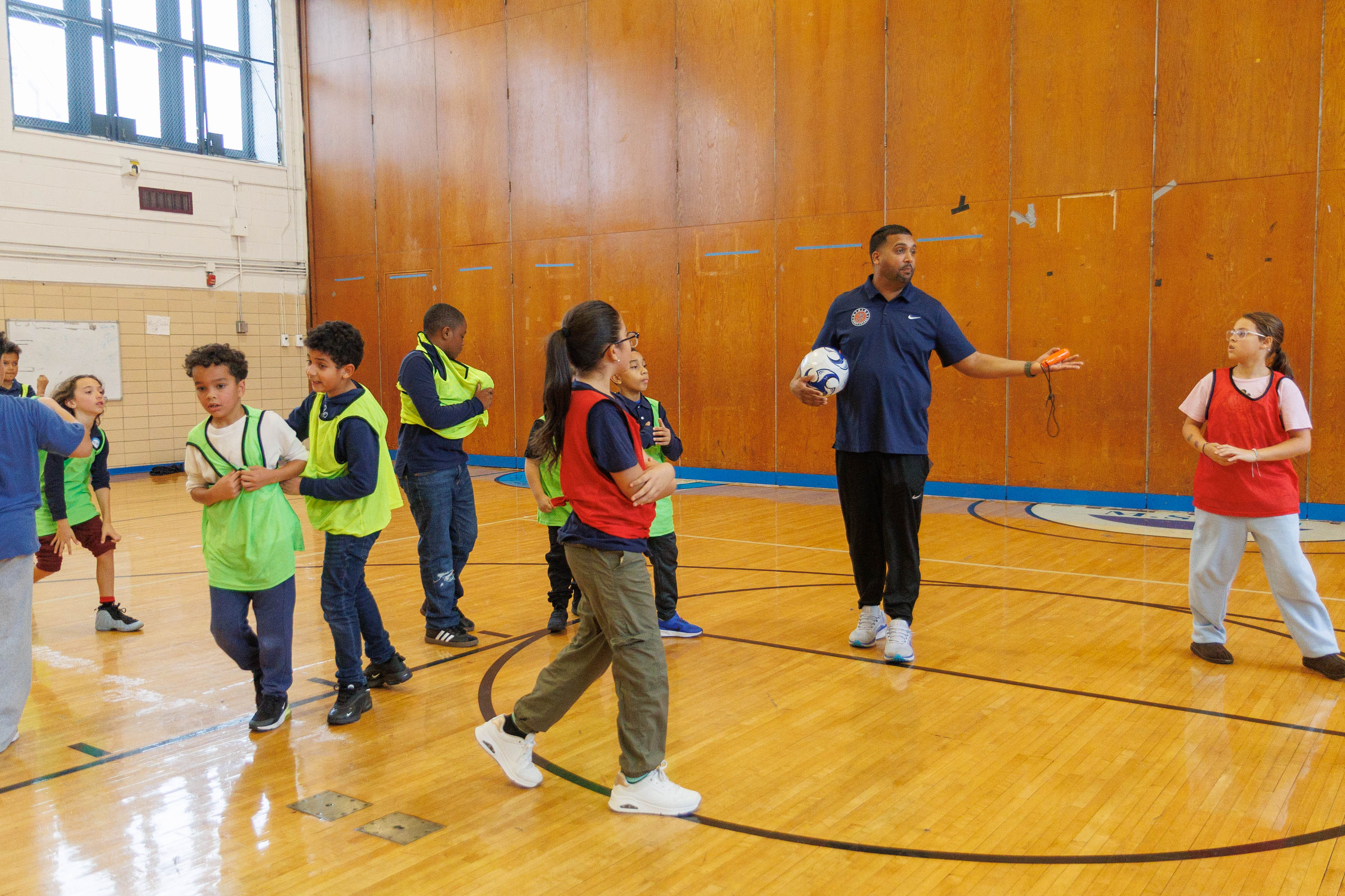 PE teacher instructing students during indoor soccer class in gymnasium