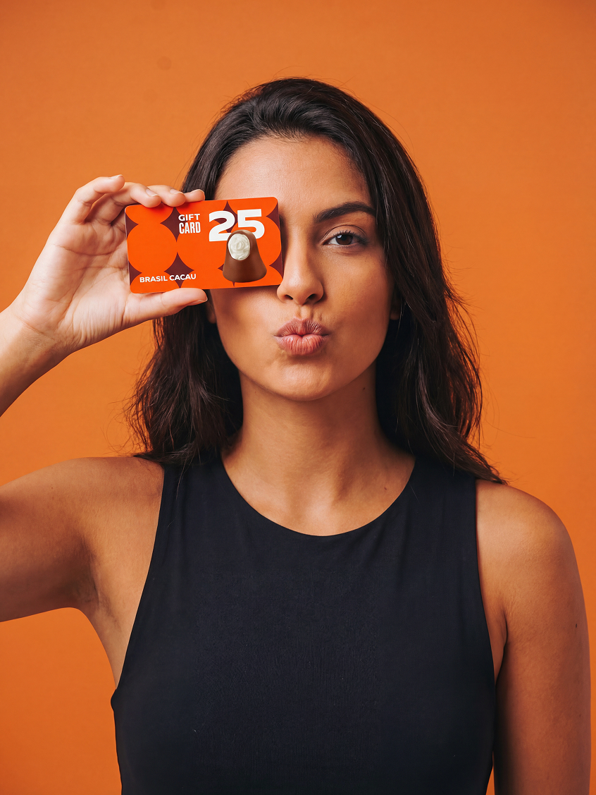 Mulher segurando cartão-presente Brasil Cacau diante do olho, sobre fundo laranja