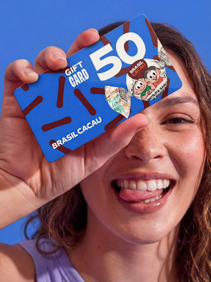 Mulher sorridente segurando gift card Brasil Cacau de 50 reais diante do rosto