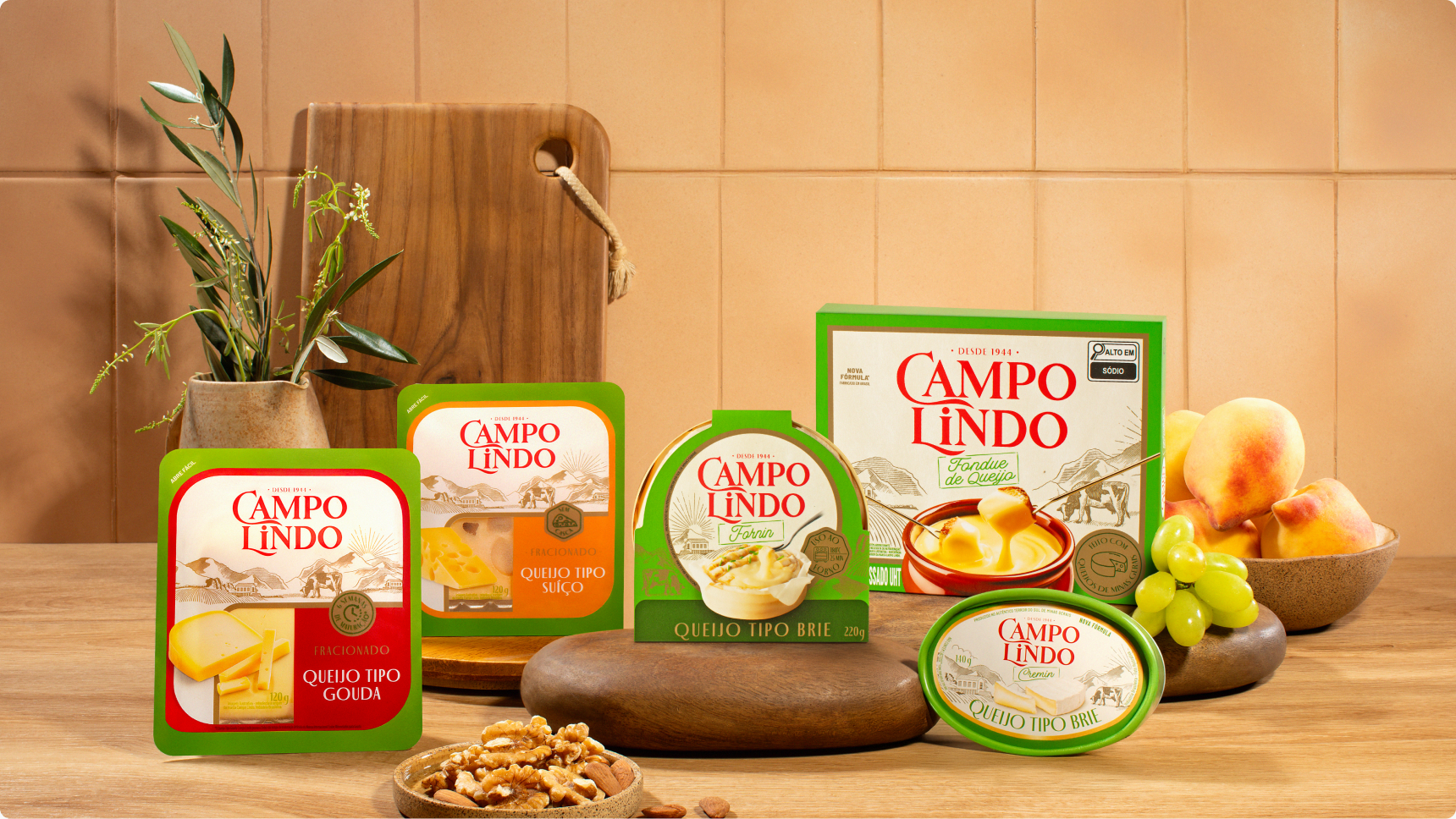 Linha de queijos Campo Lindo sobre bancada de madeira, com frutas e pães