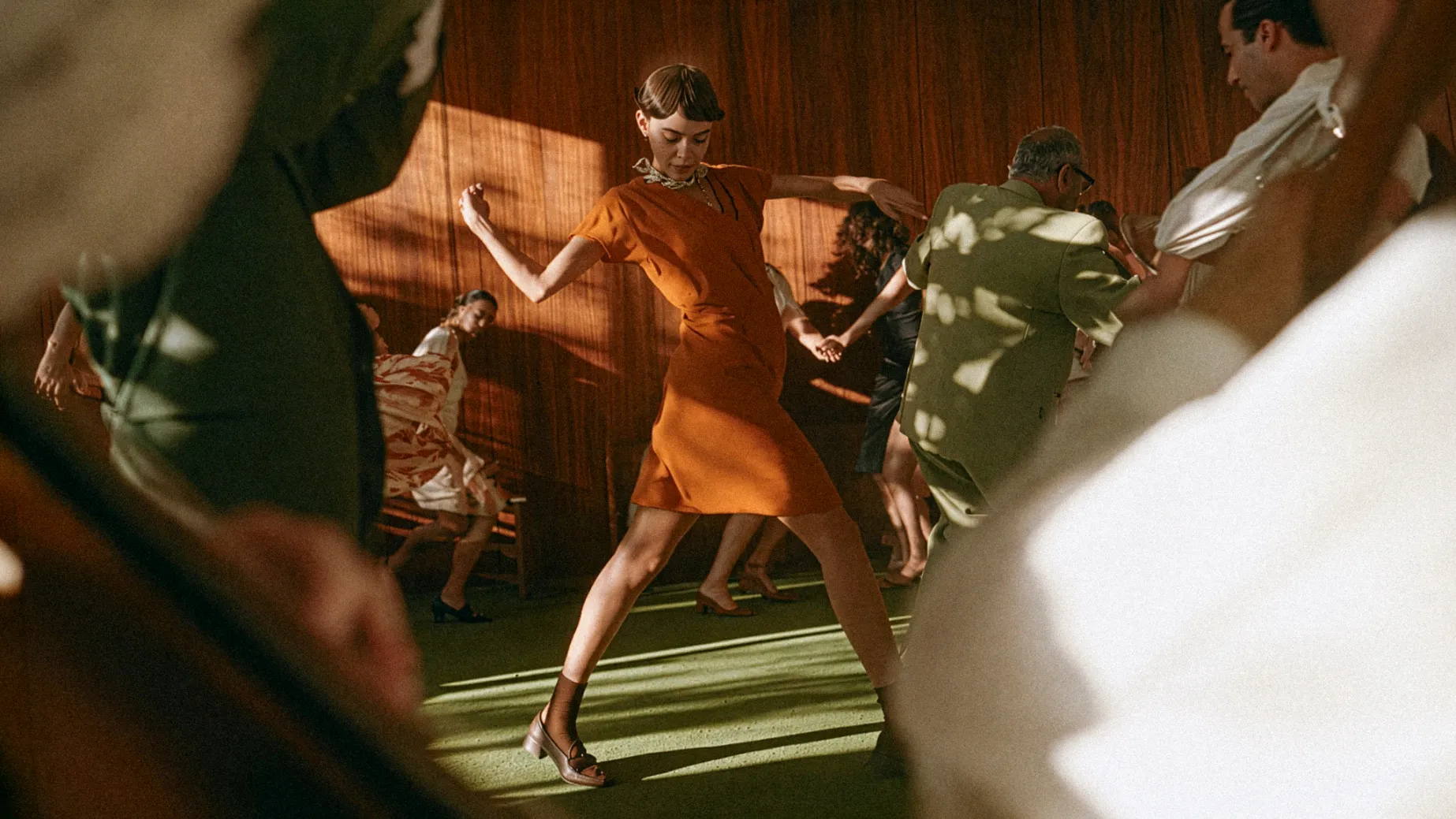 Mulher dançando com vestido laranja em salão de madeira