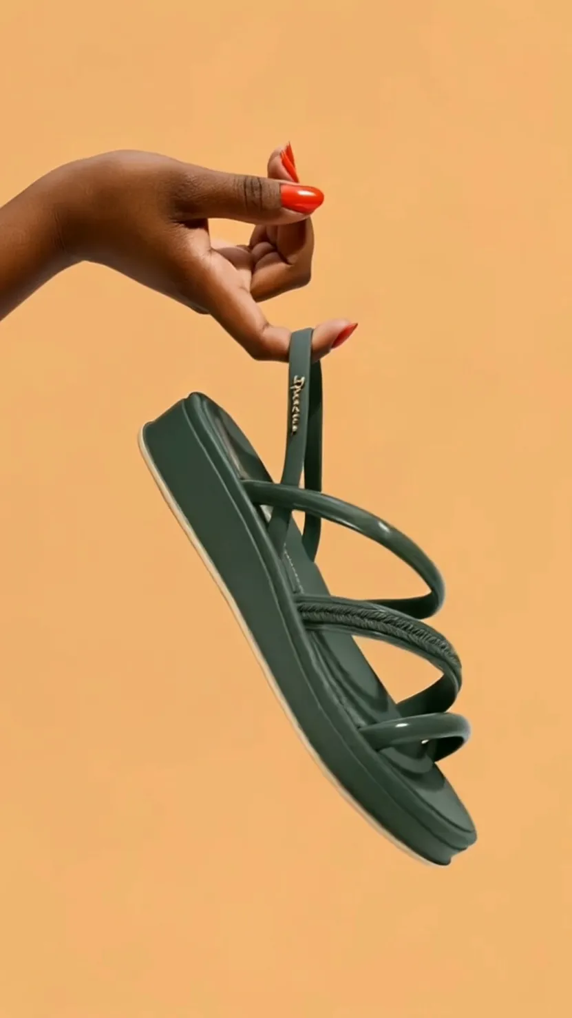 Mão segurando uma sandália verde sobre fundo laranja