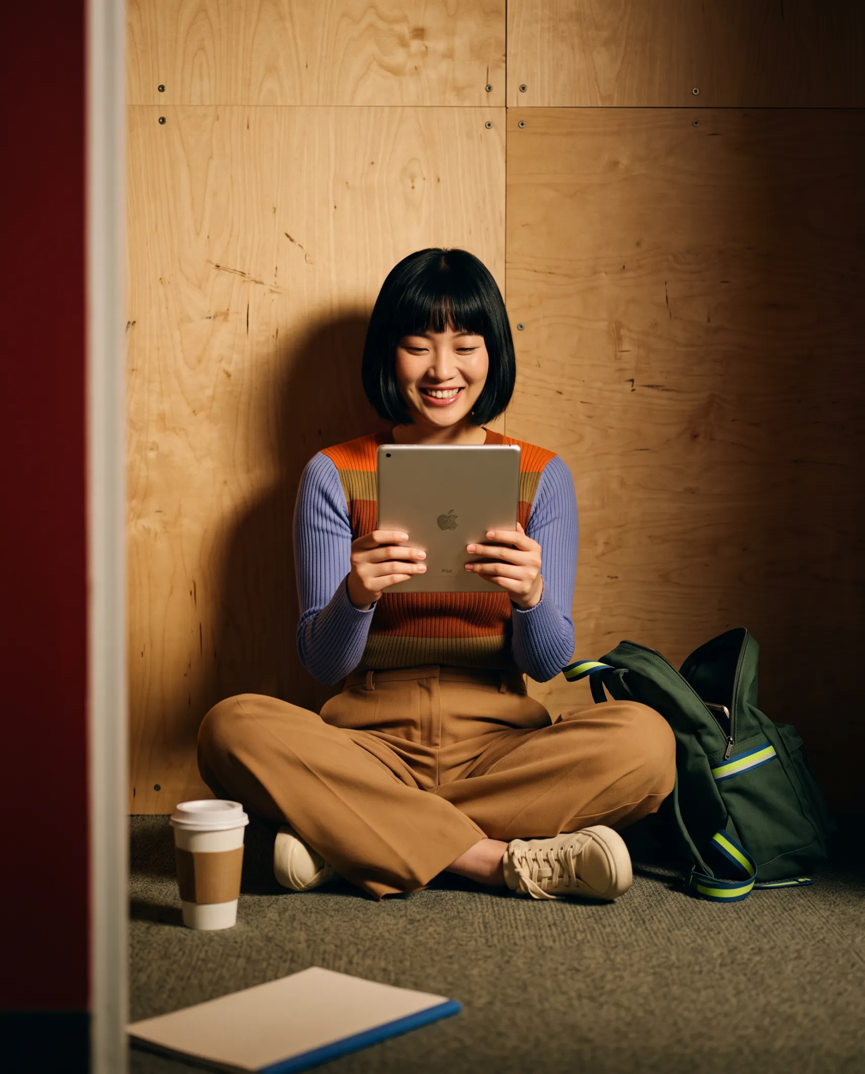 Mulher sorrindo com um tablet, sentada no chão de um estúdio