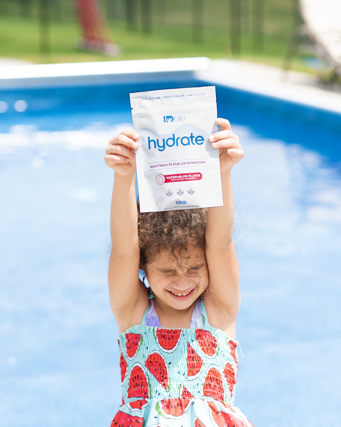 A child at a pool holding a Hydrate Watermelon bag overhead