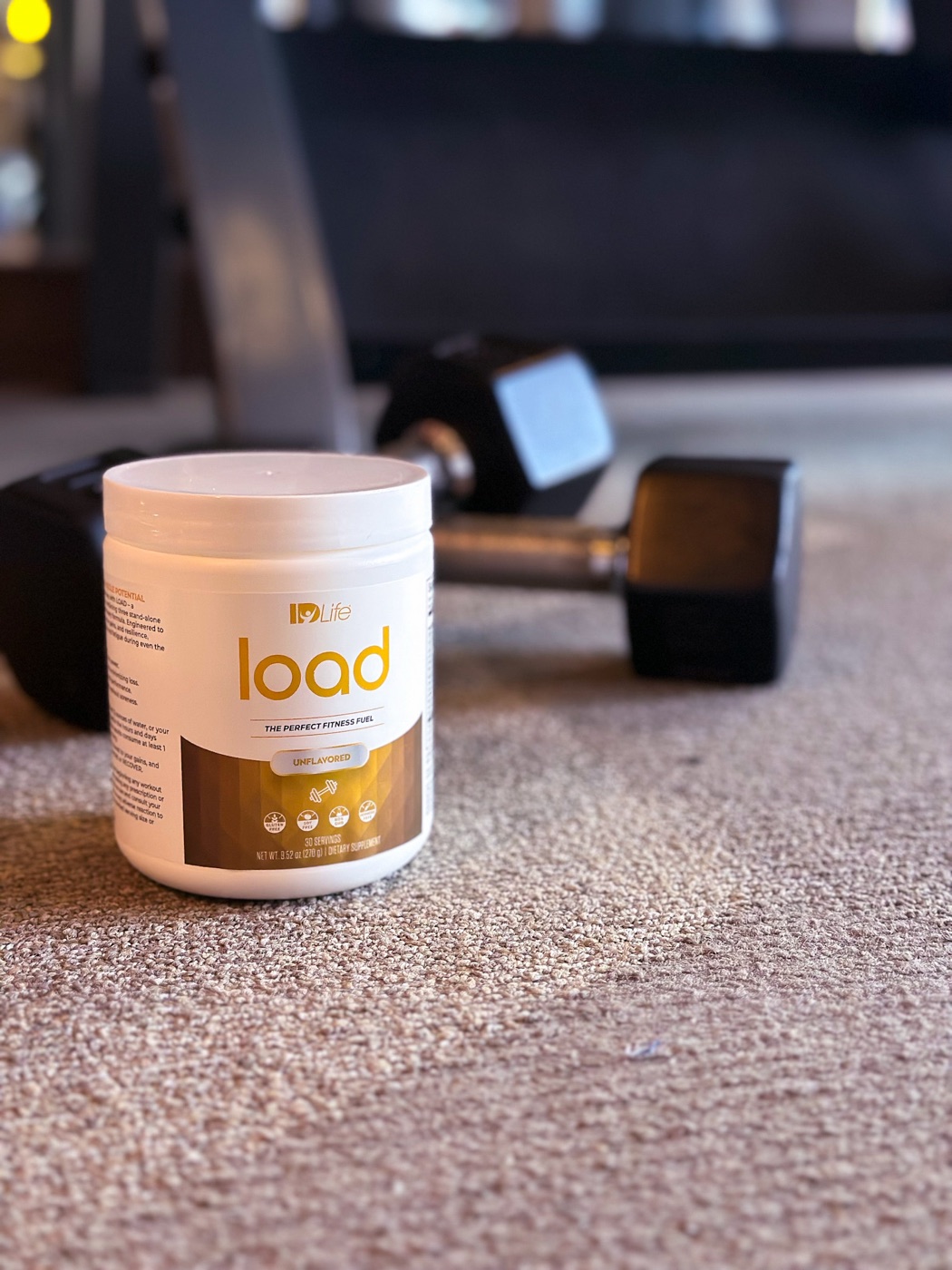 A Load jar on a home-gym floor in front of a pair of dumbbells