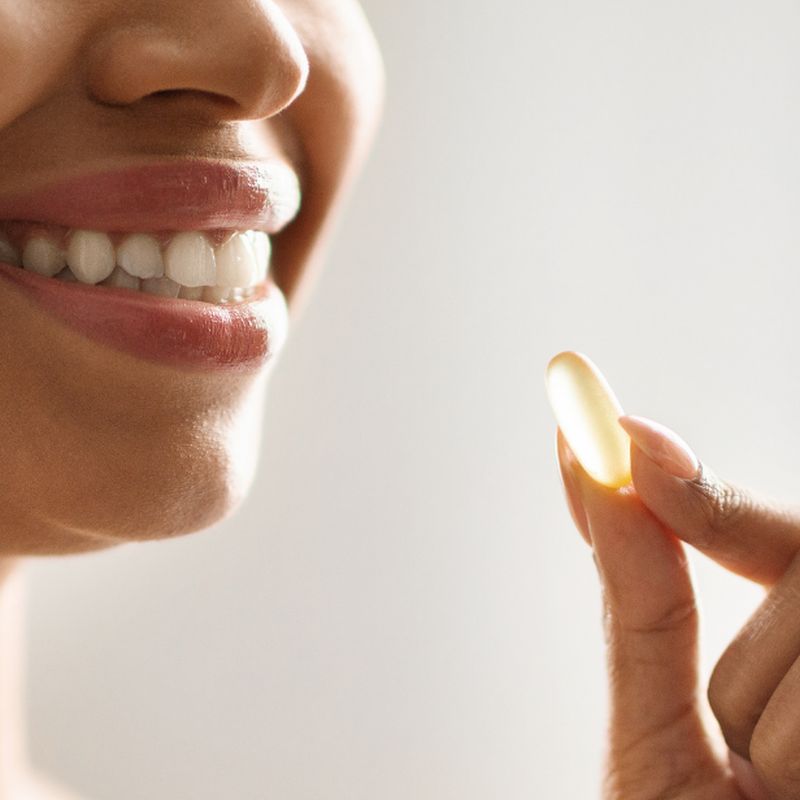 A smiling woman holding up a golden softgel between two fingers
