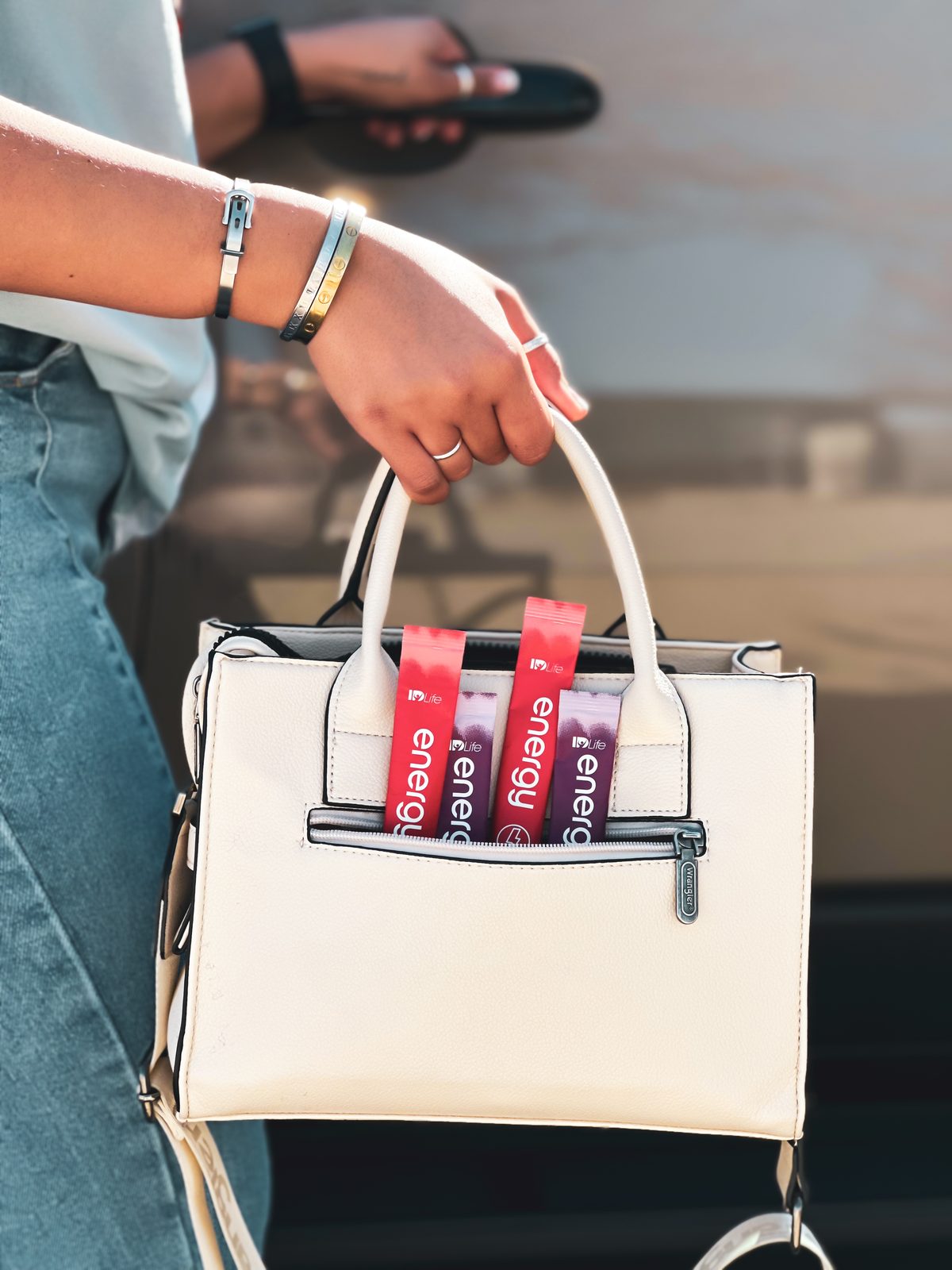 A cream handbag carried by a woman in jeans, with Fruit Punch and Mixed Berry Energy sticks tucked into the front pocket