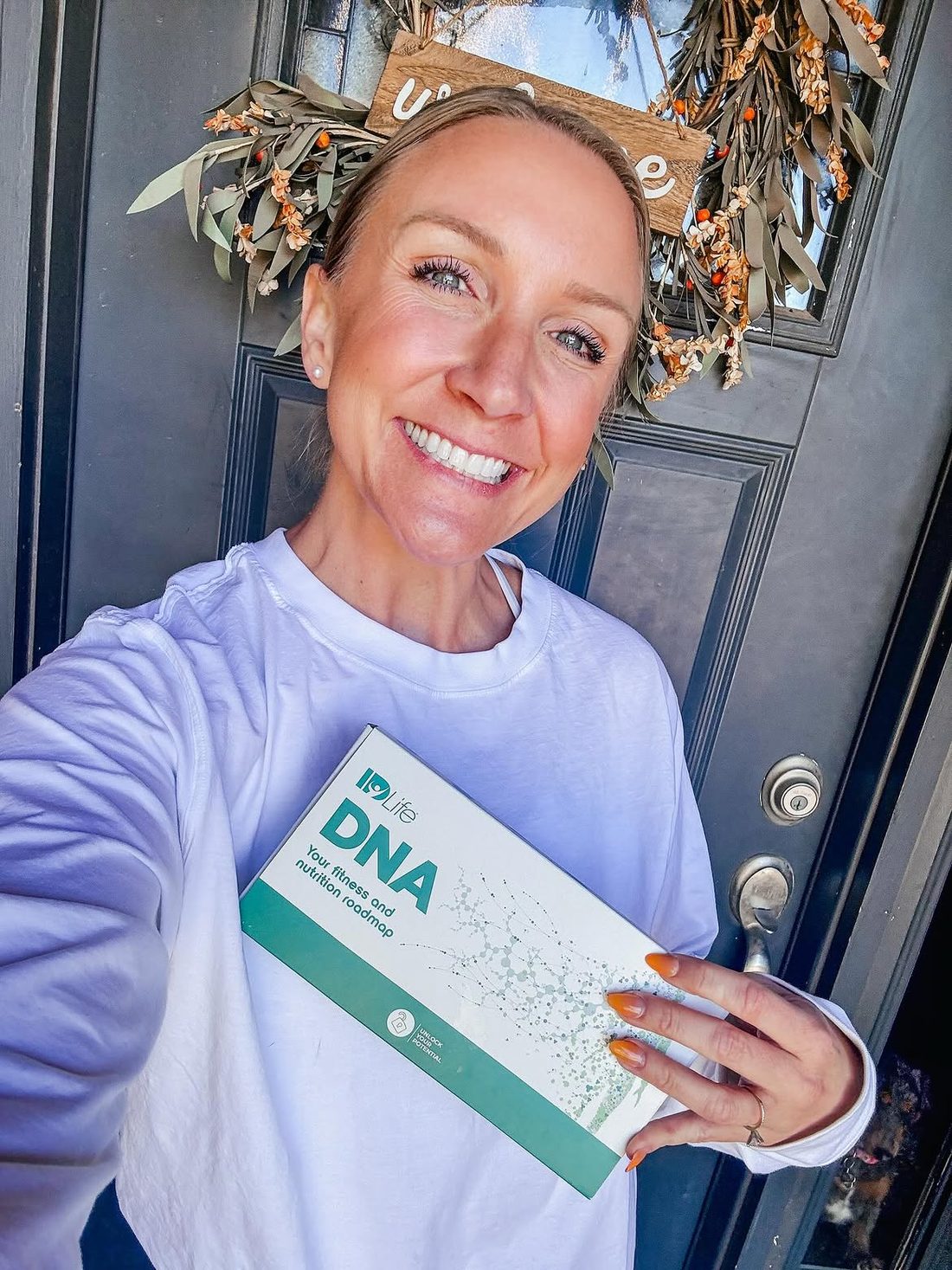 A customer smiling on her front porch holding the IDLife DNA kit she has just received
