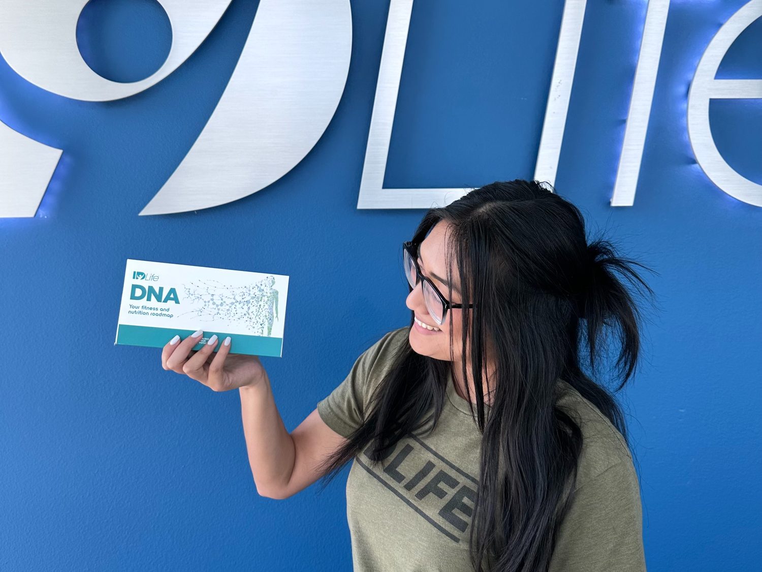 An IDLife team member holding the DNA kit in front of the IDLife sign at the company office
