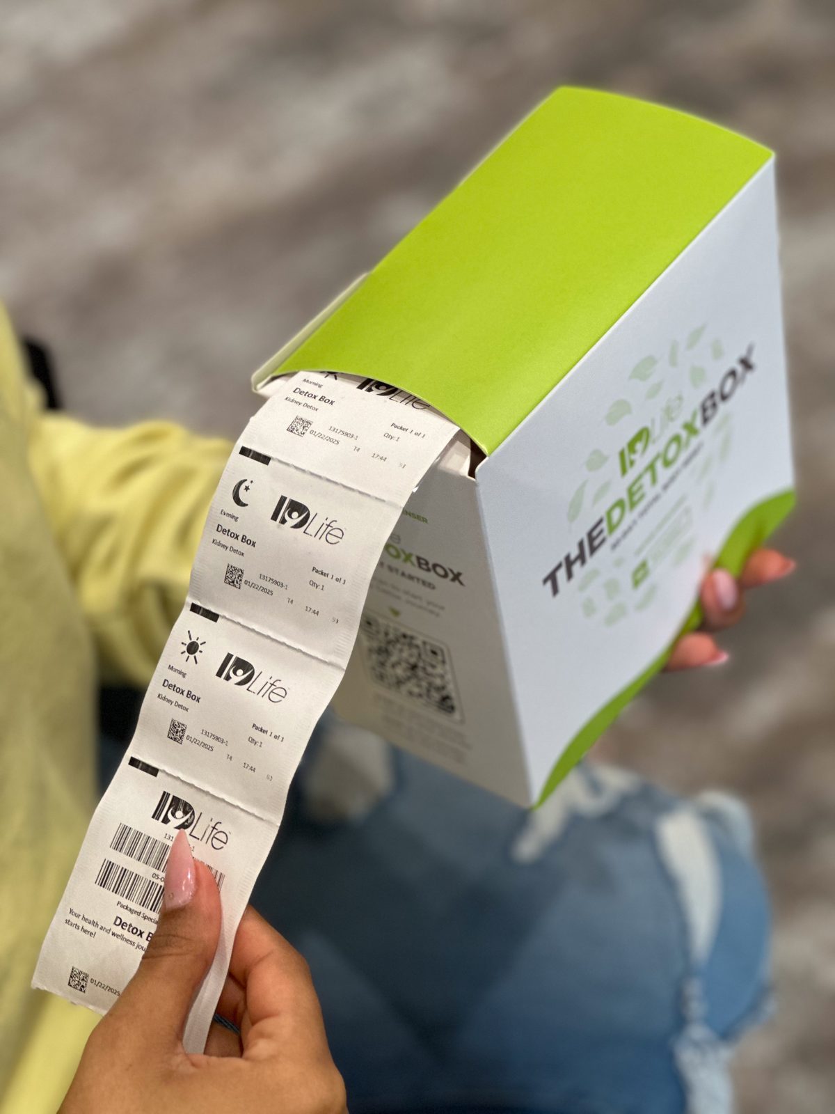 A hand pulling a strip of AM and PM Detox Box supplement packs out of the green dispenser box