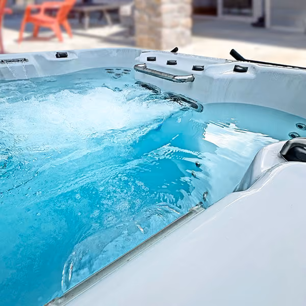 Close-up of bubbling water in a white outdoor swim spa with a stone pillar and red chair in the background.