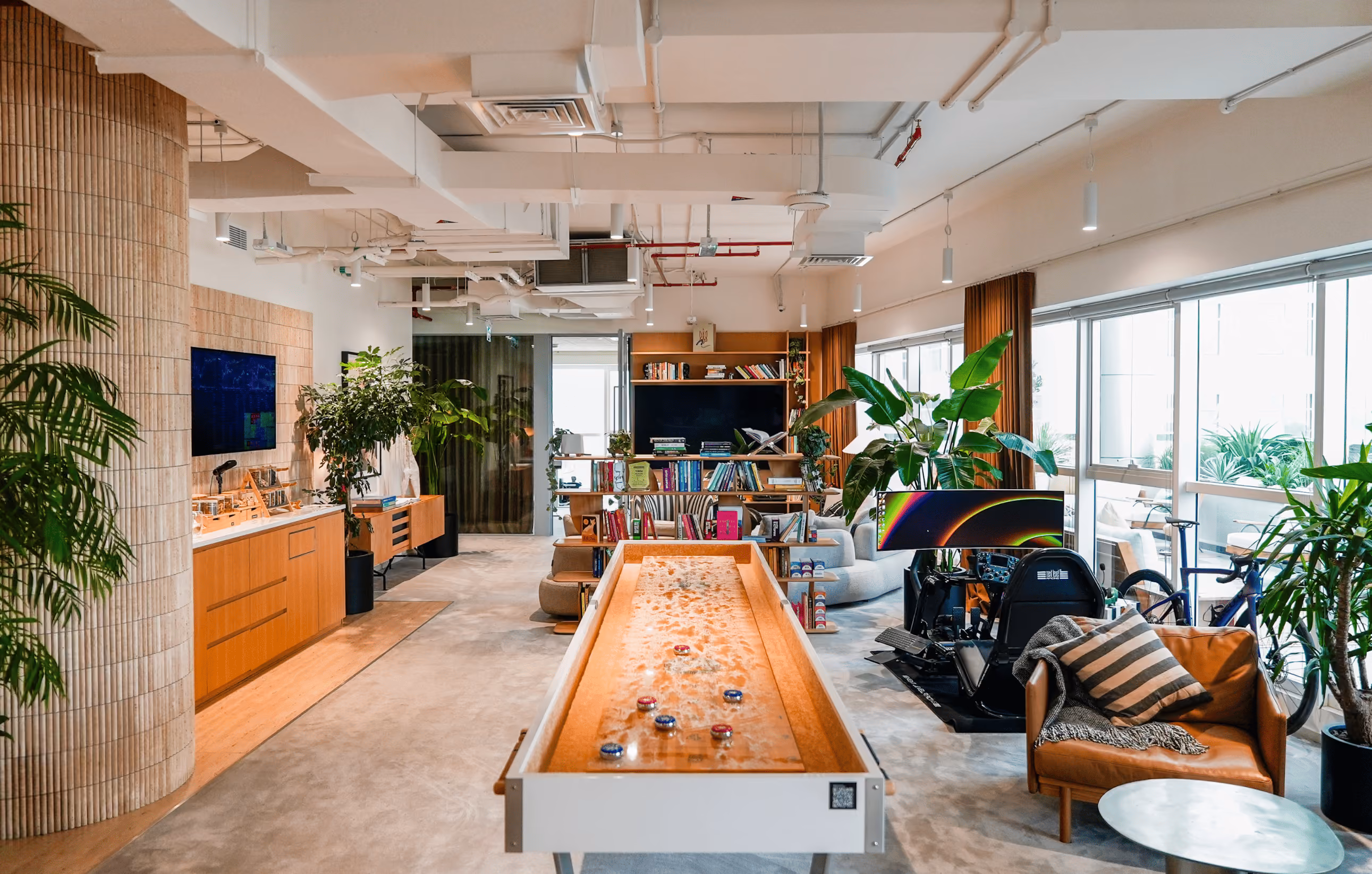 Bright modern office with wooden desks, black office chairs, computer monitors, and potted plants on windowsills.
