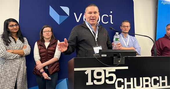 Veoci co-founder speaking at a podium.