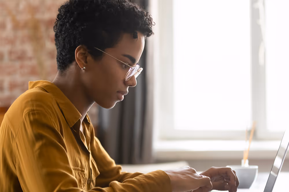 Young woman works on laptop in well-lit office.