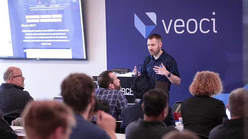 A person presenting at a podium in front of a Veoci banner.