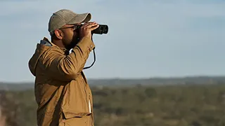 A man in a field looks through binoculars.