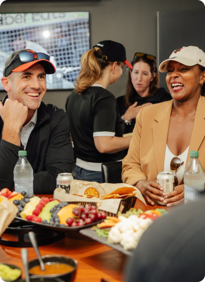 Two people smiling and talking by a table with snacks and drinks at a casual indoor gathering.