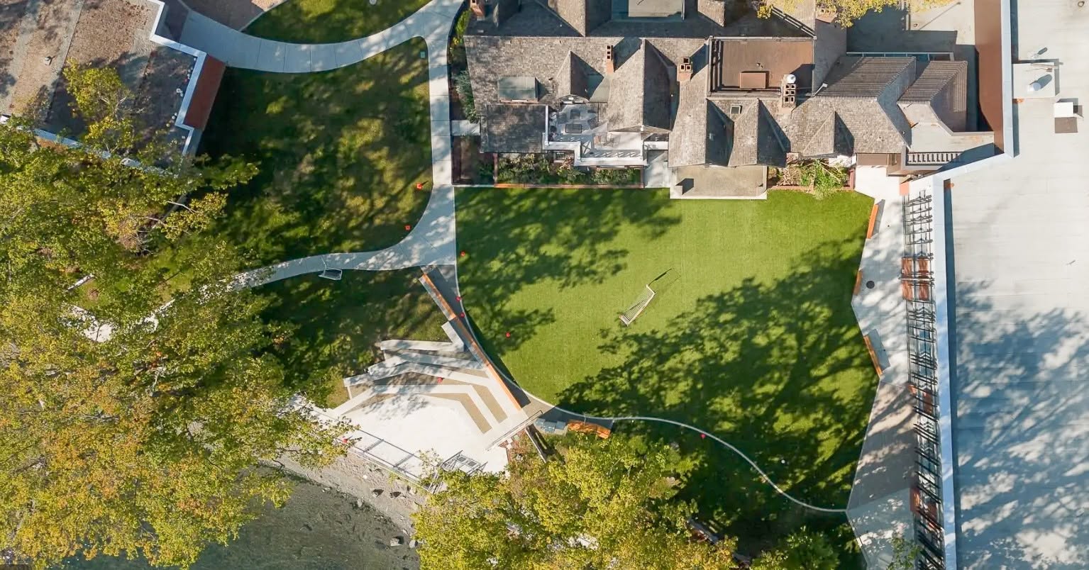 Aerial view of a housing courtyard with a green lawn, curving paths and mature trees