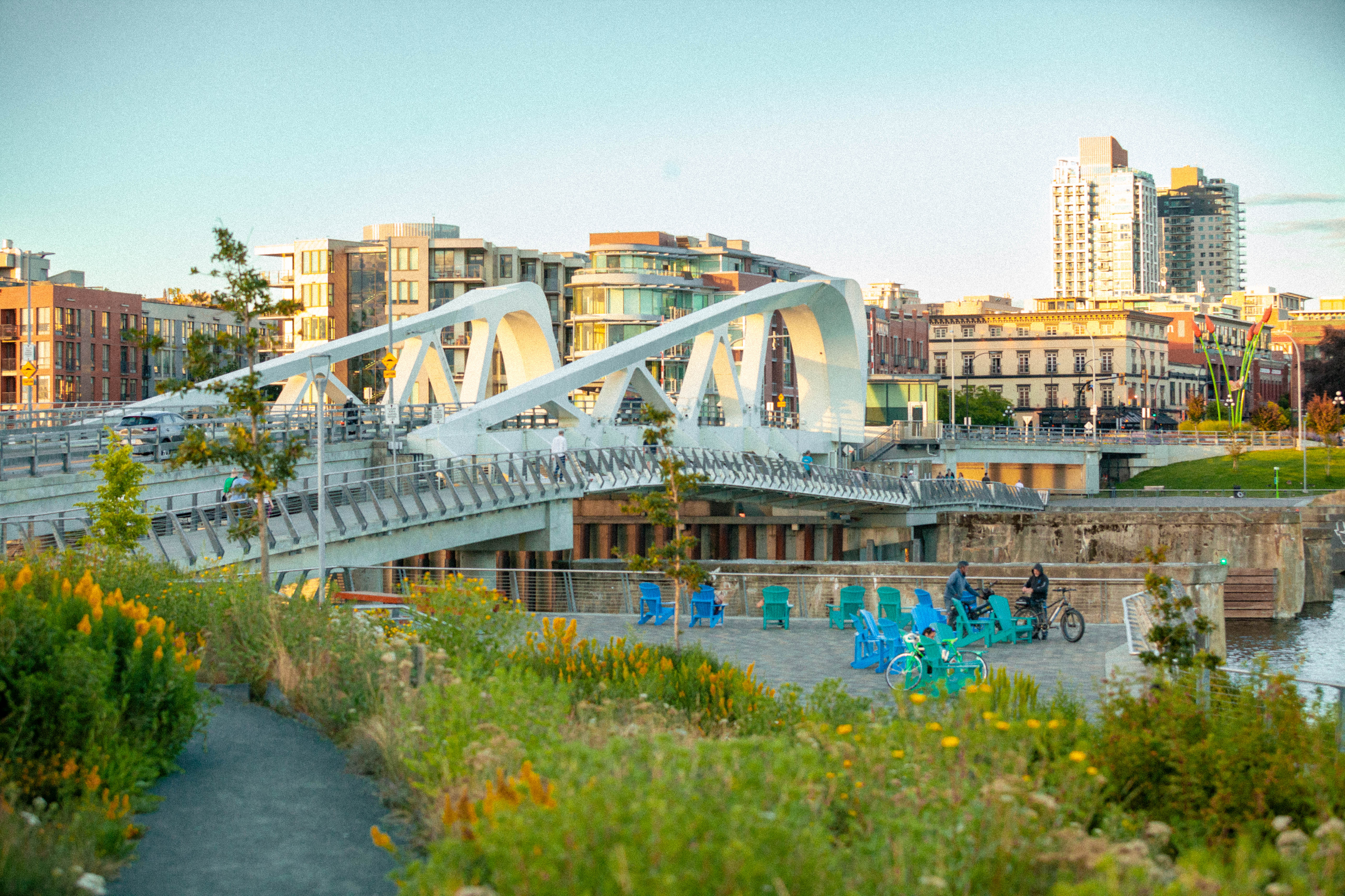 Waterfront promenade with blue chairs, cyclists and a steel bridge in downtown Victoria, BC