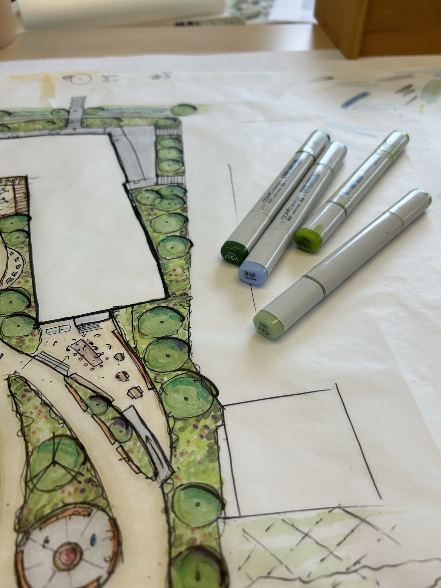Hand-drawn site plan being coloured on trace paper, with Copic markers resting on the drawing.